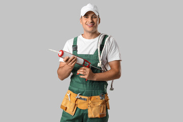 Male plumber with caulking gun on light background