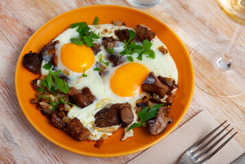 Close up of fried eggs with mushrooms and greens at plate on table