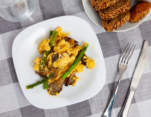Scrambled eggs with mushrooms and asparagus served on plate with silverware.