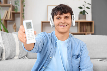 Handsome young man in headphones turning on air conditioner at home, closeup