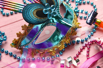 Beautiful carnival mask with party horns, confetti and beads on pink wooden background. Closeup