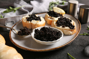 Bowl and baguette slices with delicious black caviar on dark background
