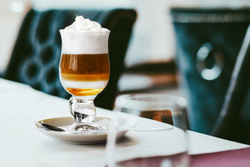 Aromatic coffee with syrup and whipped cream in a glass stands on a table in the restuarant. An idea for a sweet coffee dessert.