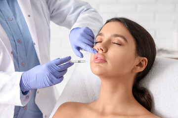 Young woman receiving filler injection in lips in clinic