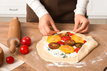 Woman preparing tasty tomato galette on table in kitchen