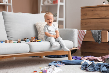 Baby boy crying on sofa in messy room