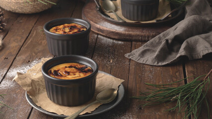 Three ramekins of creamy custard with a caramelized sugar crust, on a rustic wooden table with pine branches
