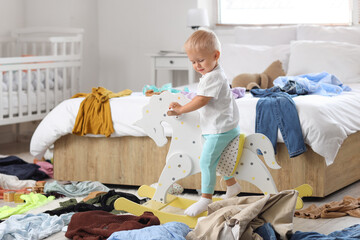 Naughty baby boy on rocking horse in messy bedroom