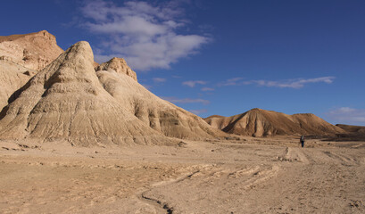 Majestic landscape of a mountain region in the Negev Desert. Orange sandstone hills and mountain folds. White clouds on blue sky. Female tourist in a hiking trail in a wide valley. Active lifestyle.