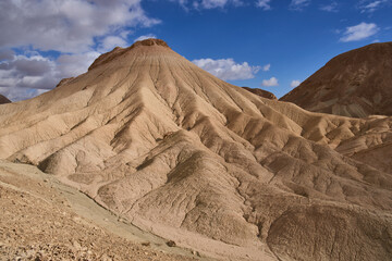 Majestic landscape of a remote mountain region in the Negev Desert. Close up view of orange sandstone hills and mountain folds. White clouds on blue sky.