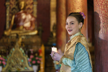 A gracefully dressed Thai woman stands serenely in the temple, illuminating the space with a...