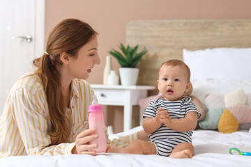 Mother with bottle of milk and her little baby in bedroom