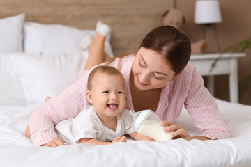 Young mother with bottle of milk and her little baby lying in bedroom
