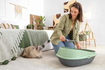 Young woman with British Shorthair cat cleaning litter box in bedroom