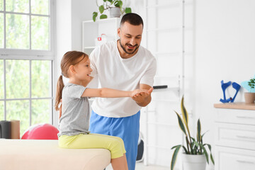 Obraz premium Male physiotherapist working with little girl on couch in rehabilitation center