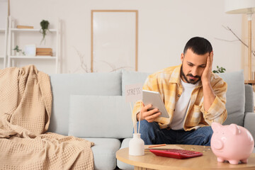 Stressed young man with tablet computer counting money at home