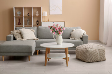 Vase with beautiful magnolia flowers on table near grey sofa in stylish living room