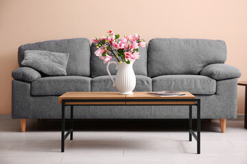 Vase with beautiful magnolia flowers and magazine on wooden table near grey sofa in stylish living room