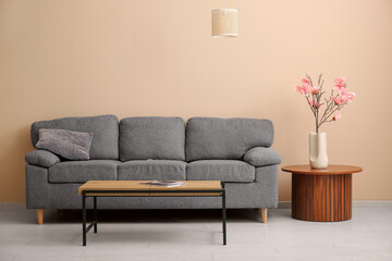 Vase with beautiful magnolia flowers on wooden table near grey sofa in stylish living room