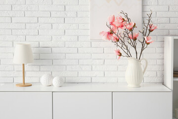 Vase with beautiful magnolia flowers on chest of drawers near white brick wall in room