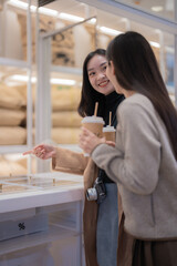 Two young women are holding takeaway coffee cups and smiling while choosing beans from a dispenser in a zero-waste store, promoting sustainable shopping and eco-conscious consumerism