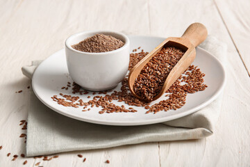 Wooden scoop with flax seeds and bowl of flour on white wooden background