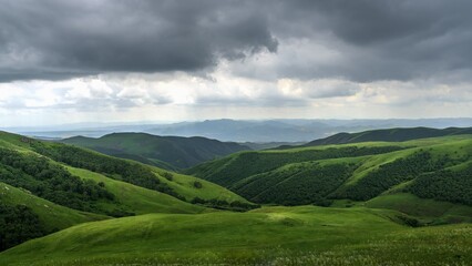 Expansive Daqingshan summer landscape in Inner Mongolia showcases lush green hills under dramatic clouds