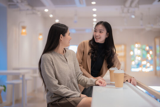 Two young women are enjoying their coffee break, chatting and smiling at a bar counter in a modern and bright cafe, creating a warm and friendly atmosphere
