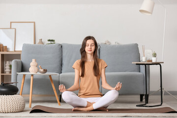 Calm young woman meditating on mat at home