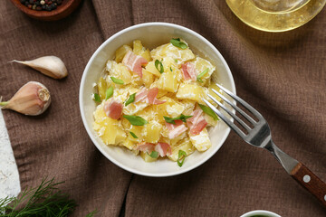 Bowl of tasty potato salad with greens, bacon and garlic on napkin