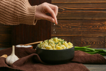 Woman salting tasty potato salad on wooden background