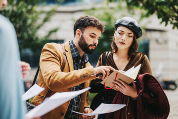 Two business professionals examine documents and take notes on a project while standing outside. The scene suggests teamwork and collaboration in a strategic business discussion.