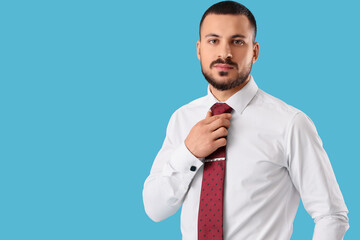 Young businessman straightening his tie on blue background