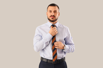 Young businessman straightening his tie on light background