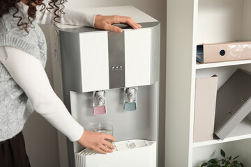 Young businesswoman pouring hot water from cooler in office, closeup