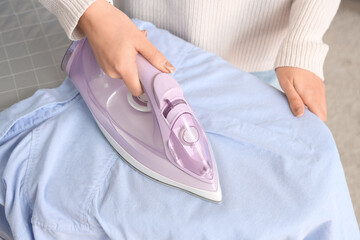 Young woman ironing blue shirt on board at home, closeup