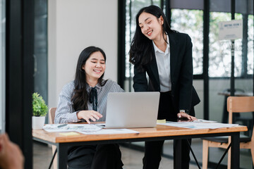 Two businesswomen working together at a desk in a contemporary office environment, discussing projects and ideas.