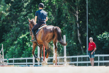 An equestrian rider in a helmet practices horseback riding in an outdoor arena. A coach observes...