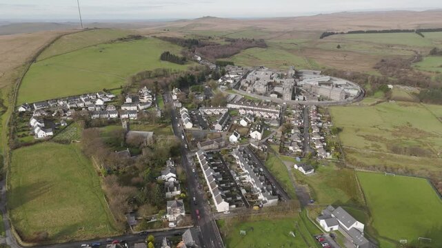 High-angle aerial of Princetown in Dartmoor, showing a rural village layout, rolling moorland, and the imposing stone-walled HM Prison Dartmoor complex