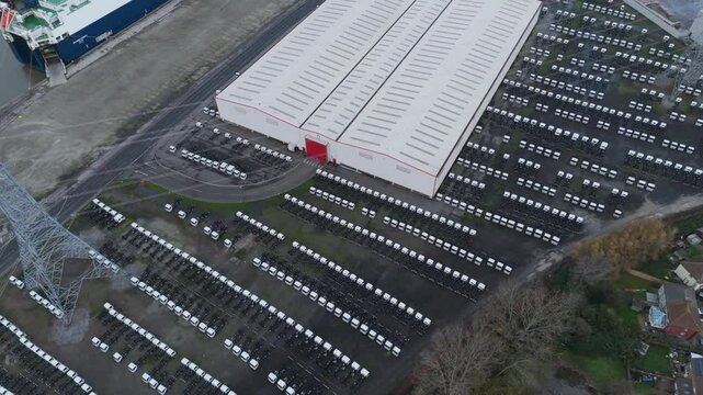 Aerial top-down view of tightly arranged imported lorries parked in rows near a large warehouse, highlighting organized commercial logistics and inventory management