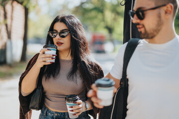 A stylish man and woman wearing sunglasses enjoy coffee while walking outside on a sunny day. They appear relaxed and happy, embodying a casual lifestyle scene.