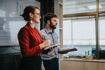 Two business people in a modern office environment discuss sales strategies, showcasing charts on a...