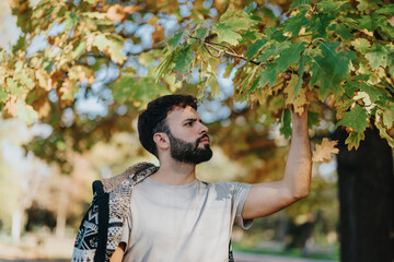 Obraz premium A man with a pensive expression examines vibrant autumn leaves in a serene park setting. The scene captures the essence of fall and outdoor exploration, highlighting a moment of nature appreciation.
