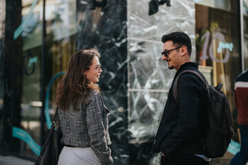 A man and a woman, dressed in professional attire, engage in conversation outside a contemporary building. They appear to be business colleagues discussing work or sharing ideas in a casual setting.