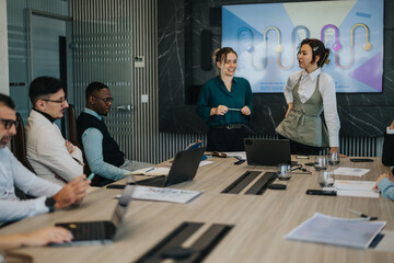 A diverse group of people engaged in a lively business meeting. Team members are seated around a...