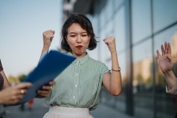 A diverse group of business professionals joyfully celebrating a successful outdoor meeting in the city. The team's positive energy and teamwork highlight their accomplished achievement. Urban