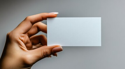 Fototapeta premium A hand holding a blank business card against a neutral background.