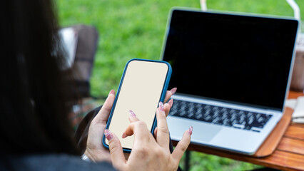Close up of female hand holding mobile phone and laptop on sunny day