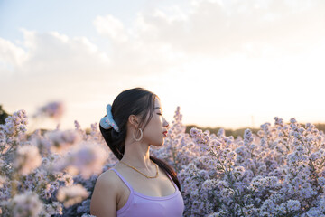 Portrait of beautiful asian girl in violet dress in cutter flower field at sunset sky.