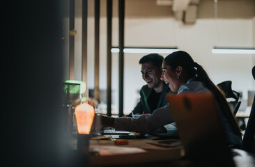 Two colleagues work together enthusiastically in an open office environment, sharing ideas and...